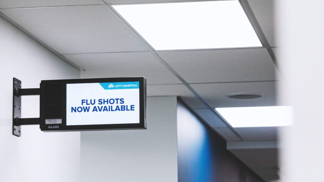 Algo IP display speaker mounted in a hospital hallway showing a flu shot announcement